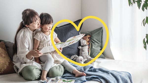 ソファで絵本を読む親子と、クッションに囲まれたぬいぐるみ。やわらかな光とテキスタイルで心地よく過ごすリビングの一角