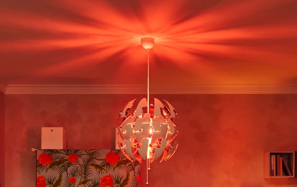 Soffitto di un soggiorno con lampada a sospensione IKEA PS che diffonde sul soffitto una luce rossa in stile discoteca