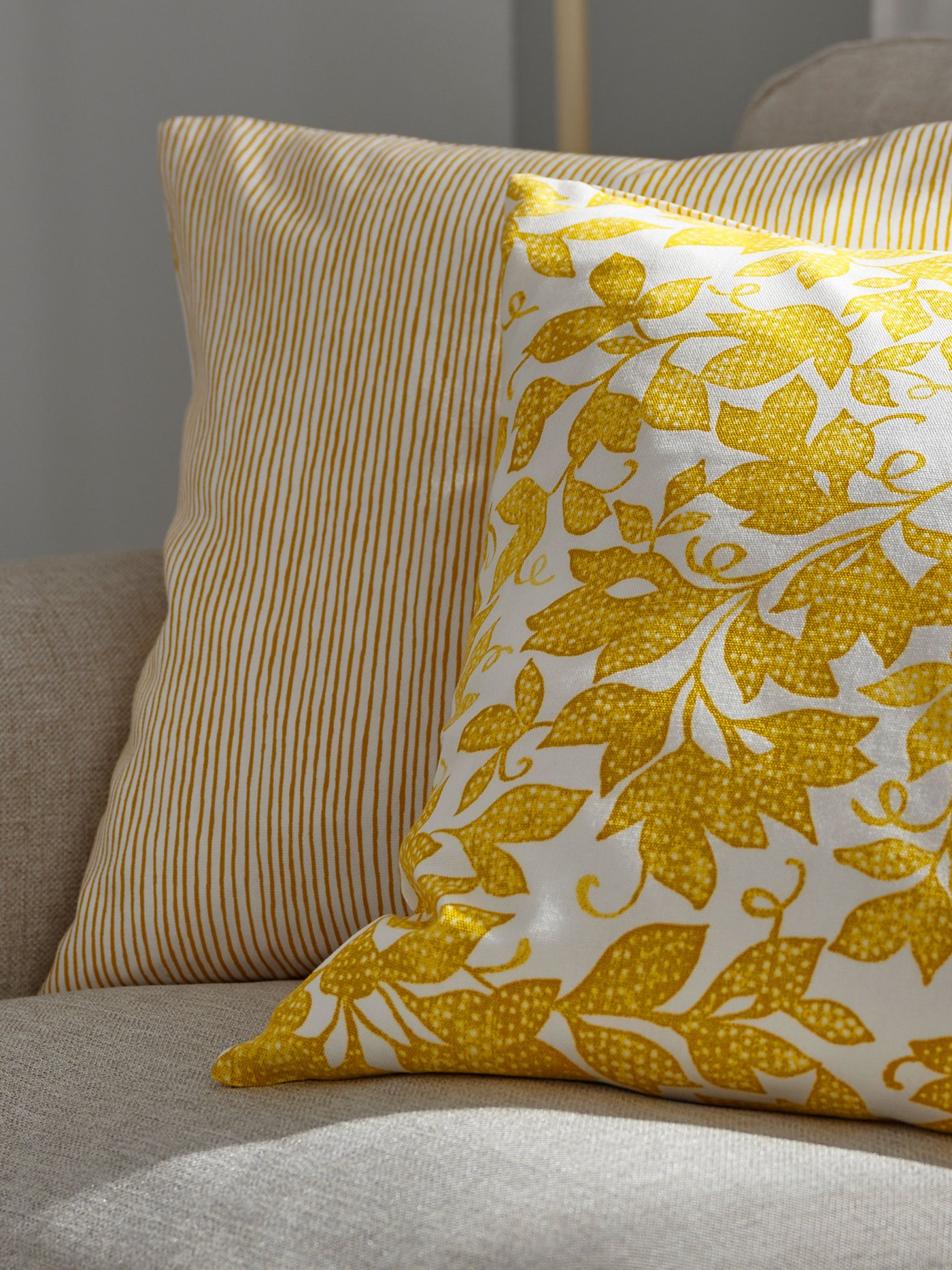 Soffkuddar i gult blommönster och randigt tyg arrangerade på en ljus soffa.
