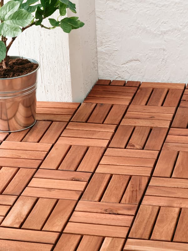 Sol en bois sur mesure pour l’espace extérieur, avec une plante en pot dans un cache-pot métallique, un mur blanc en arrière-plan.