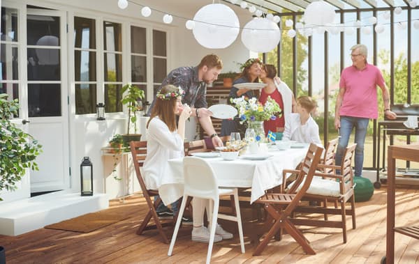 Solfyldt tagterrasse med mennesker omkring et bord, der er pyntet med blomster, hængende lanterner og små svenske flag.