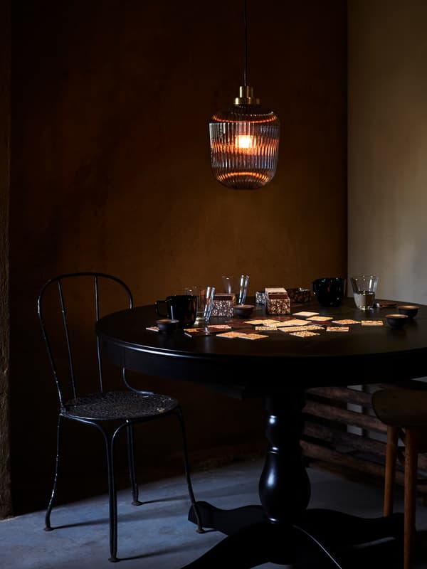 SOLKLINT pendant lamp made in grey glass lighting up a dark room, hanging above a round black table with a card game.