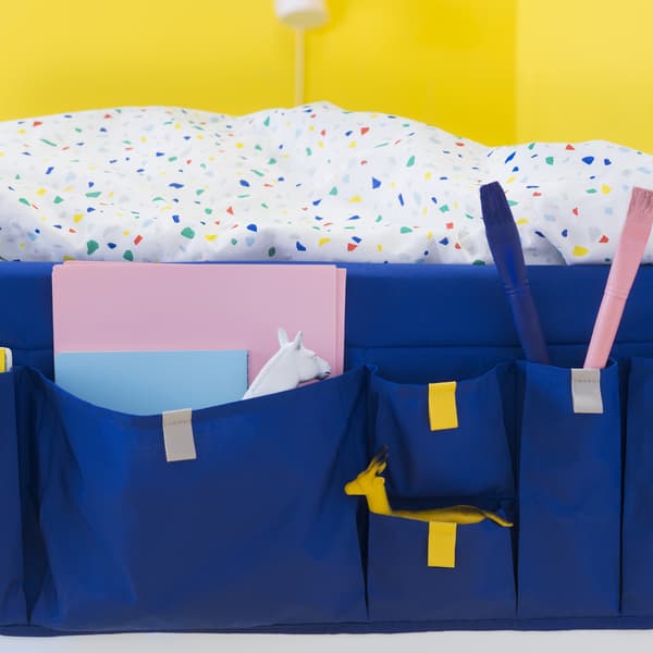Some colourful bedding and a blue bed pocket filled with notebooks against a yellow background.
