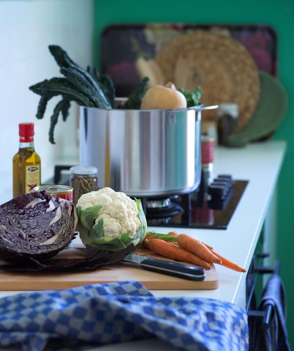 Some vegetables on a work surface beside a cooking hob with a large saucepan.