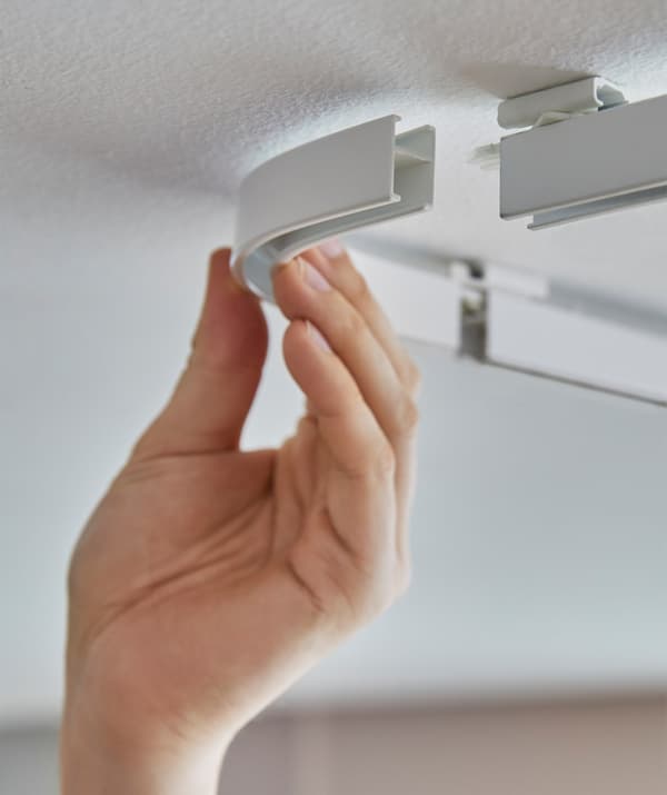 Someone clicking together the corner pieces of an IKEA VIDGA track system mounted on the ceiling.