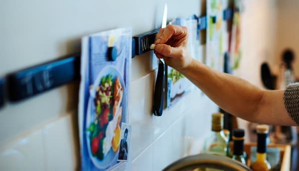Someone writes the day of the week on a knife rack painted with chalkboard paint.