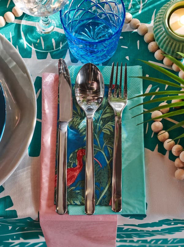 มีด ส้อม และช้อน วางอยู่บนงานปะต่อ SOMMARLIV และกระดาษเช็ดปาก FANTASTISK/ฟันทัสติสค์ เป็นส่วนหนึ่งของการจัดโต๊ะสำหรับงานรื่นเริง