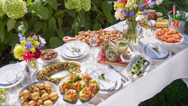 Sommerlich gedeckter Gartentisch mit vielfältigen Speisen, frischen Blumensträußen und IKEA-Geschirr – ideale Inspiration für Gartenpartys und festliche Mahlzeiten im Freien.