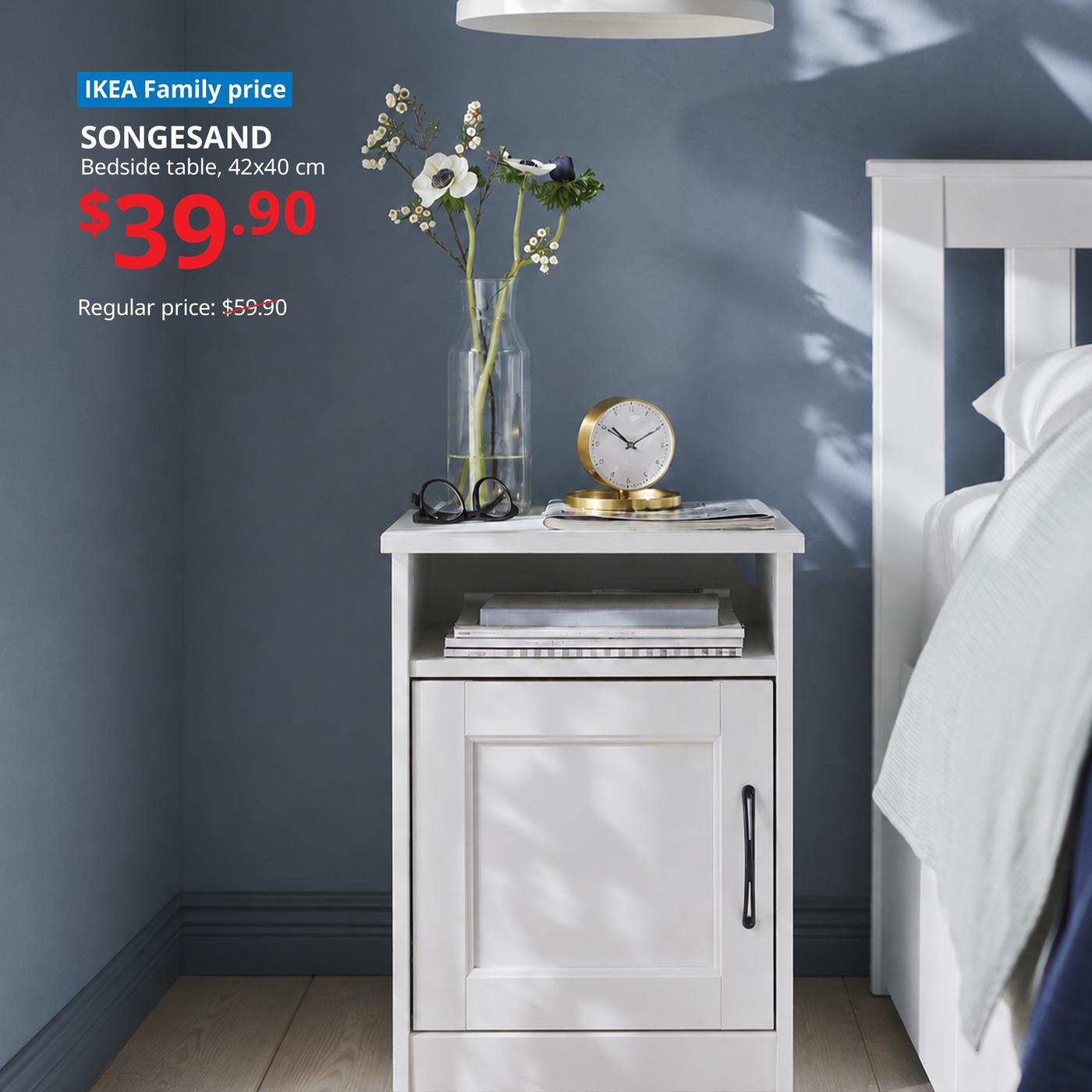 SONGESAND bedside table next to a white bedframe, with a vase of flowers, a clock and books. Words on image read "IKEA Family price, SONGESAND, Bedside table, 42x40 cm, $59.90, regular price $39.90."