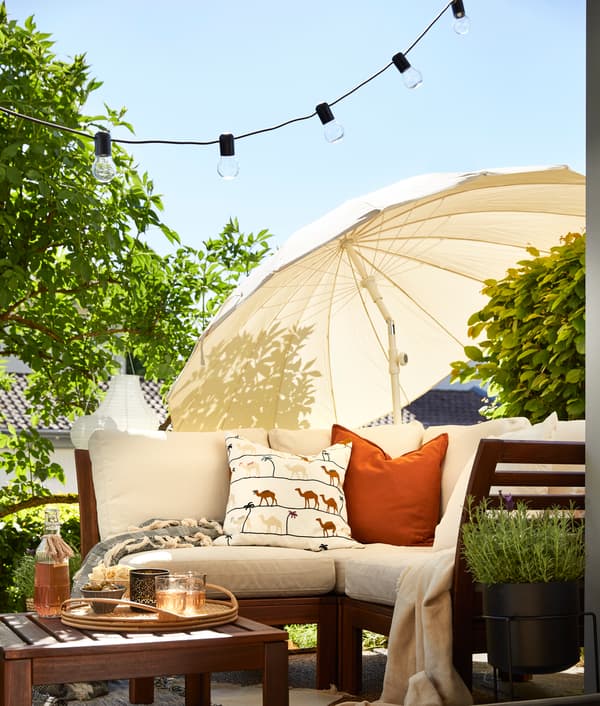 Sonnige Terrasse mit Gartenlounge aus Holz und Sonnenschirm