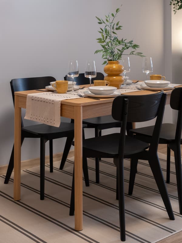 Современная обеденная зона с деревянным столом, черными стульями, нейтральной посудой и теплым рассеянным освещением.