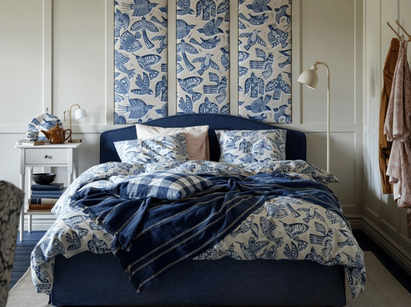 Sovrum i vitt och blått med blå sänggavel och mönstrad textil, pläd, påslakan och kuddar i blått och vitt.