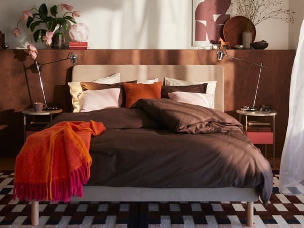 .Sovrum med en bäddad säng i bruna och röda toner omgiven av lampor och dekorationer.