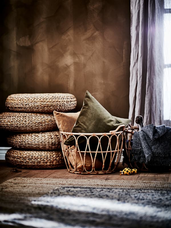 Spálňa v zemitých hnedých farbách s hnedou stenou, ratanovými košmi SNIDAD, stoličkami ALSEDA a kobercami z prírodných materiálov. 