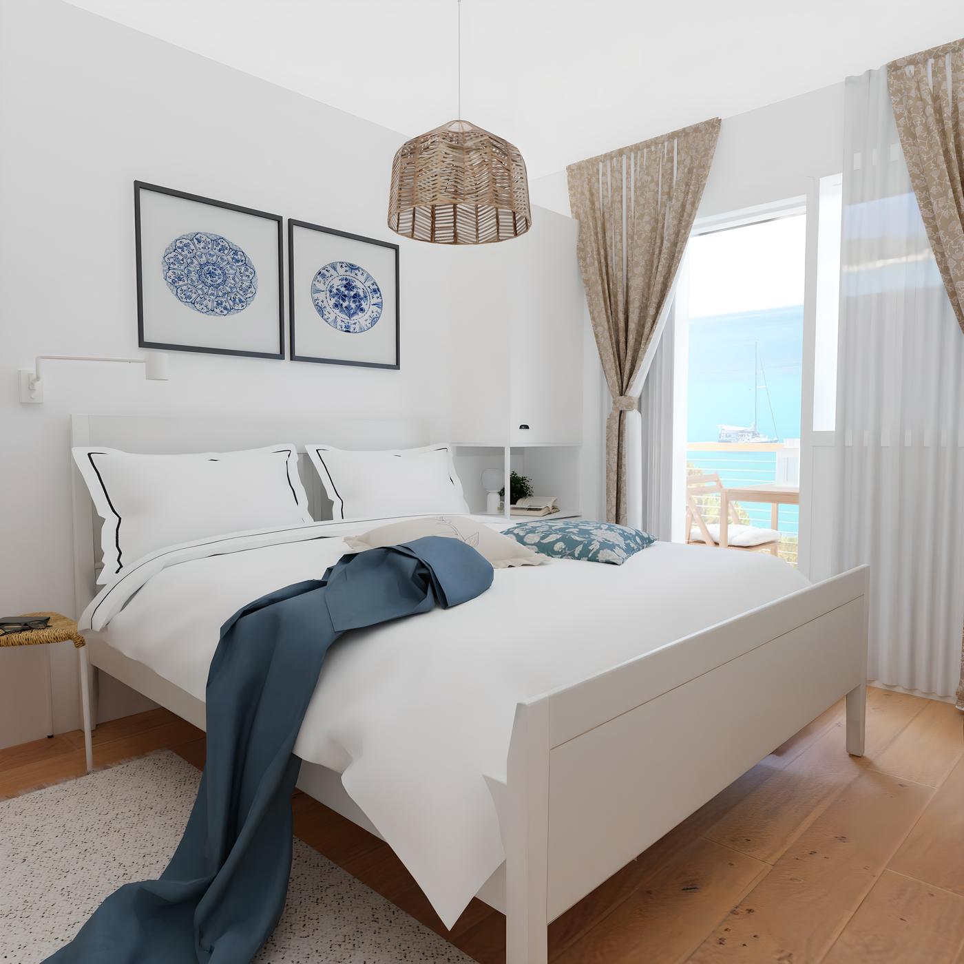 Spavaća soba s bijelim krevetom, plavim pokrivačem, dvije slike na zidu, prozor s pogledom na more i zavjesama.