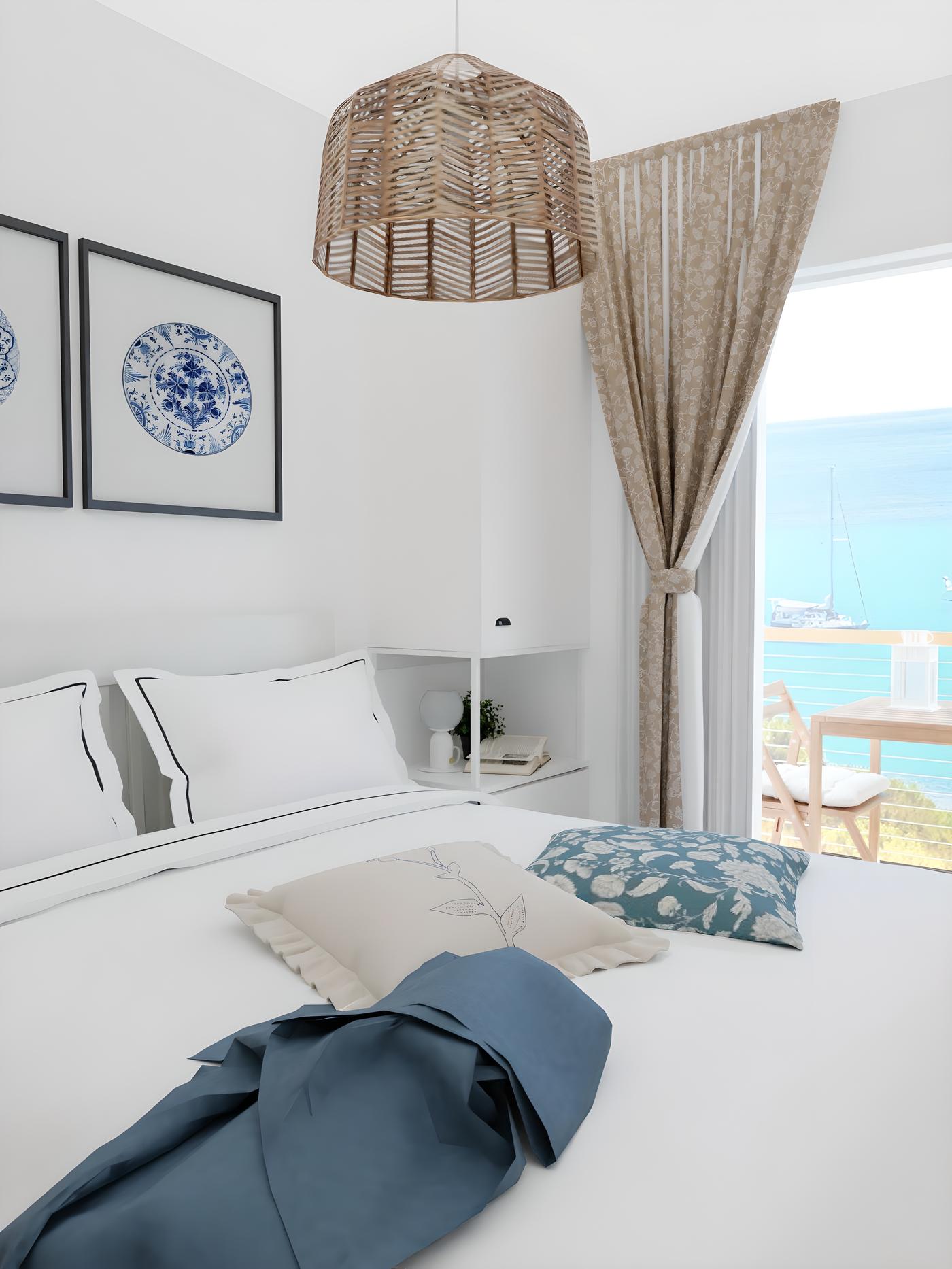Spavaća soba s bijelim zidovima, krevetom s bijelom posteljinom i plavim jastucima, te pogledom na more kroz prozor.