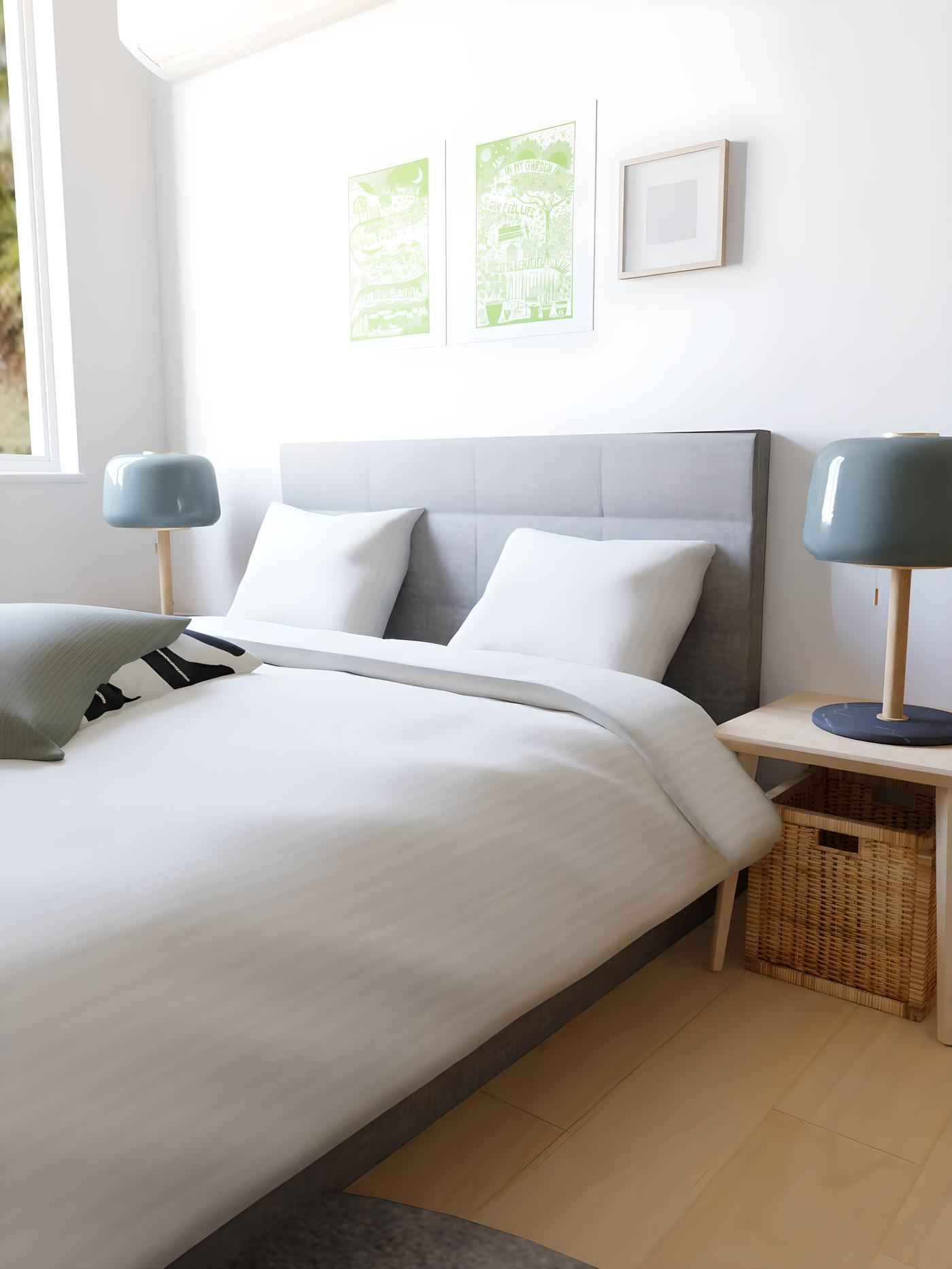Spavaća soba s bijelim zidovima, sivim krevetom, bijelom posteljinom, plavim lampama i dvije zelene slike iznad uzglavlja.