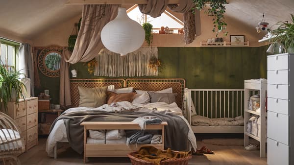 Spavaća soba s boho atmosferom i bračnim krevetom, prekrivenim neutralnom posteljinom i jastučićima, pored kog je beli GULLIVER krevetac.