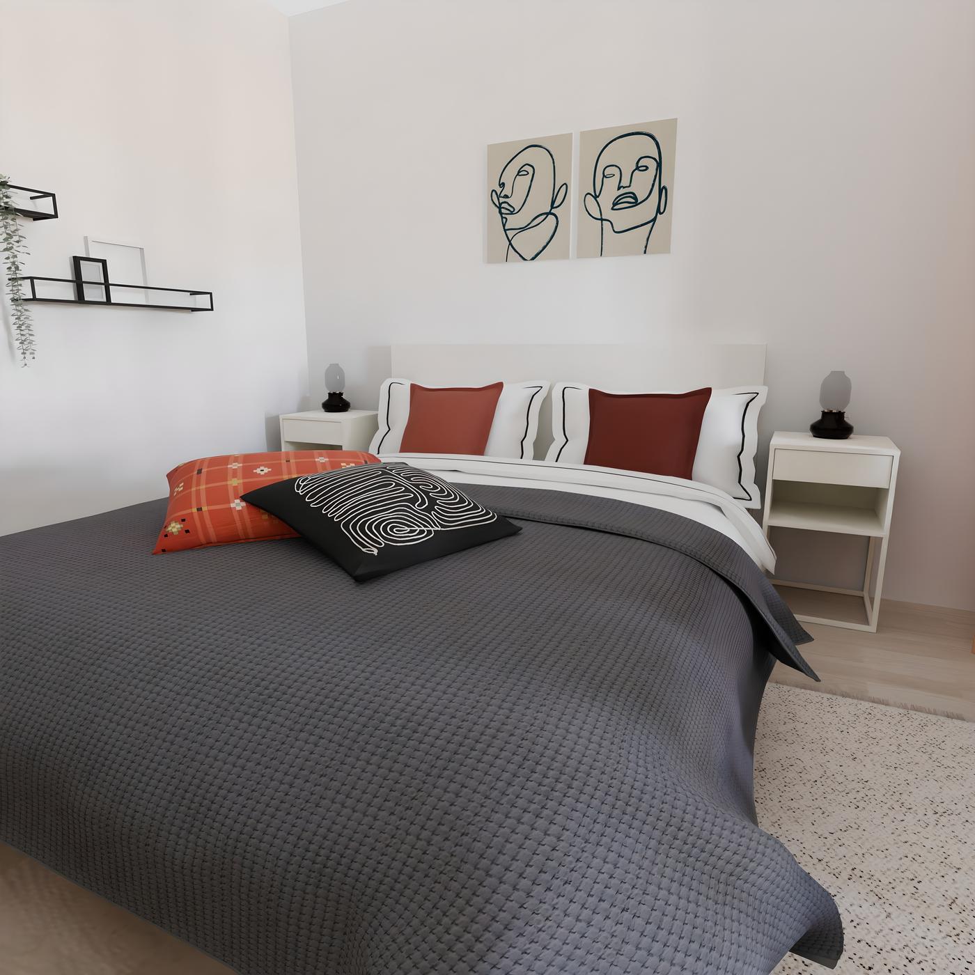 Spavaća soba s krevetom, sivom posteljinom, crnim i narančastim jastucima te dvije slike apstraktnih lica na zidu iznad kreveta.