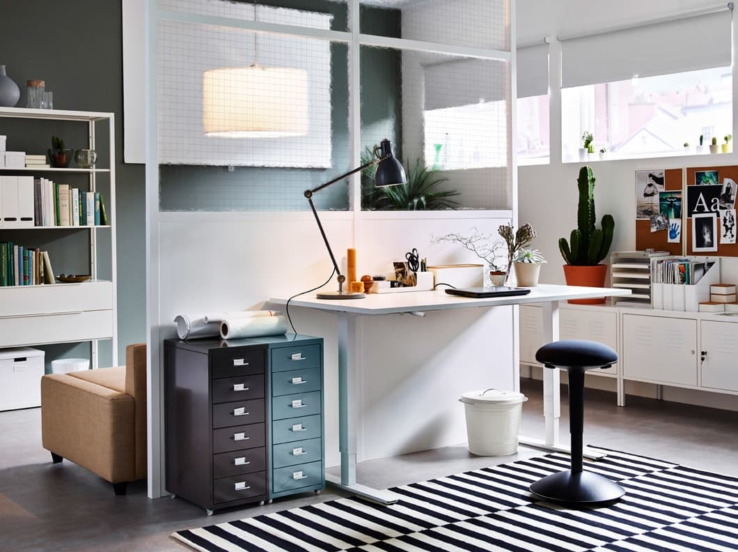 Spazio di lavoro con scrivania bianca regolabile in altezza, sgabello nero e cassettiere in grigio e verde. - IKEA