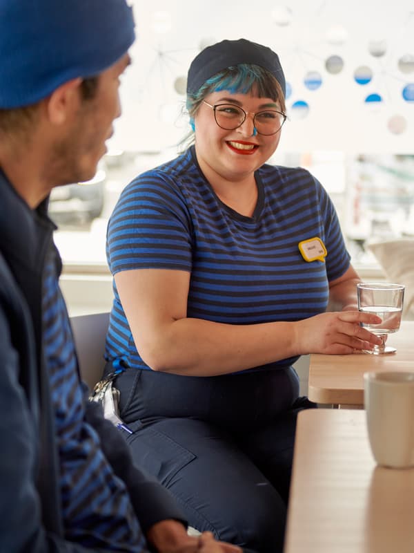 Співробітник і співробітниця IKEA з блакитним волоссям, яка п’є воду в їдальні для персоналу.