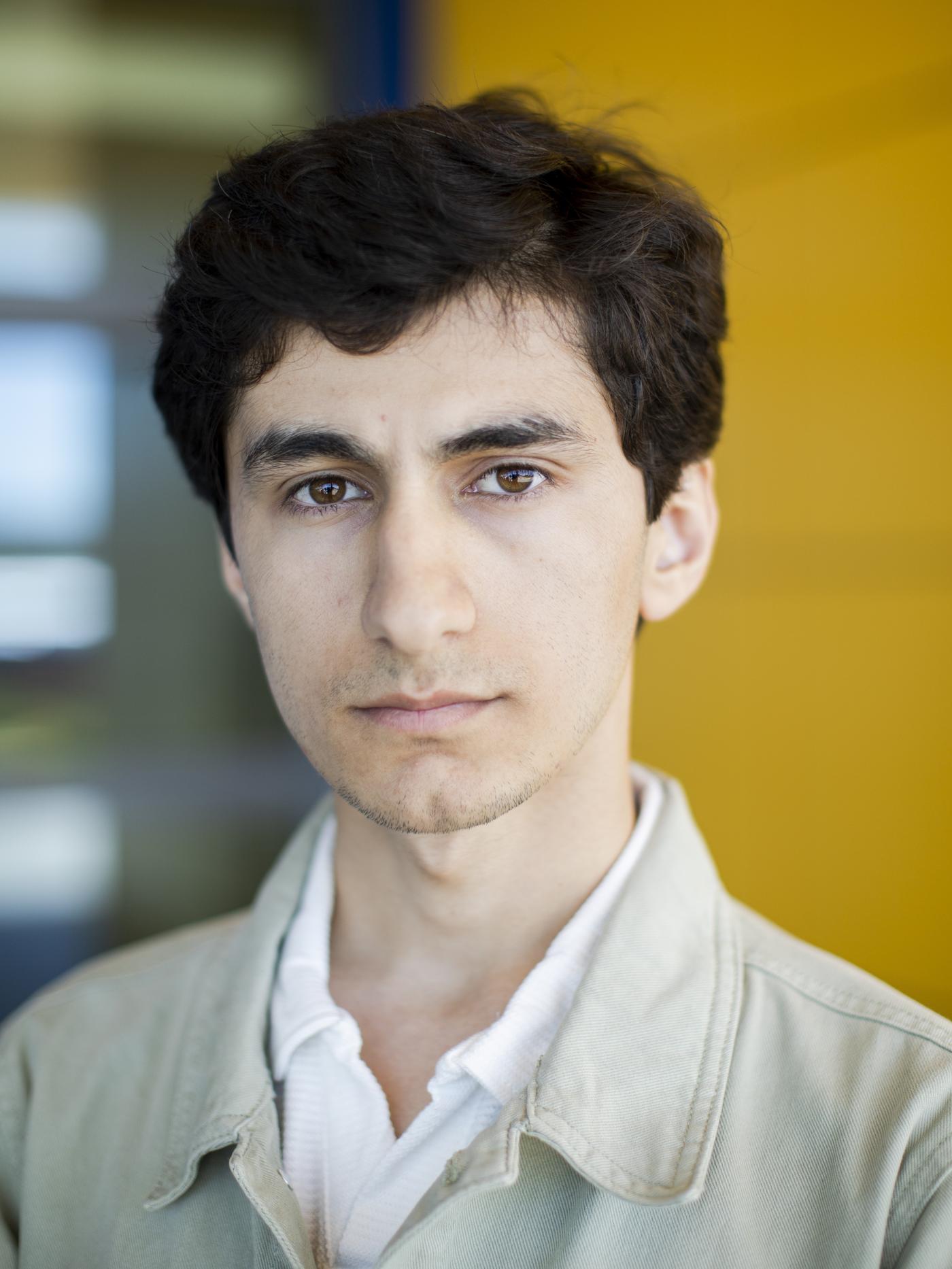 Spokojny Ali z Tadżykistanu ubrany w białą koszulę i kremową marynarkę patrzy w kamerę. 