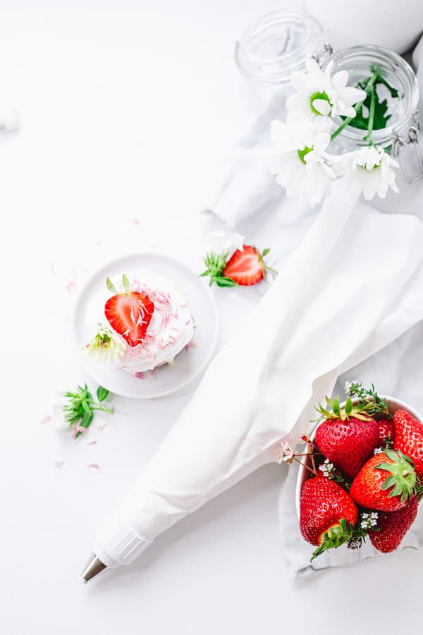 Spritzbeutel, Schale mit Erdbeeren und kleines Dessert mit Erdbeeren auf weisser Oberfläche.