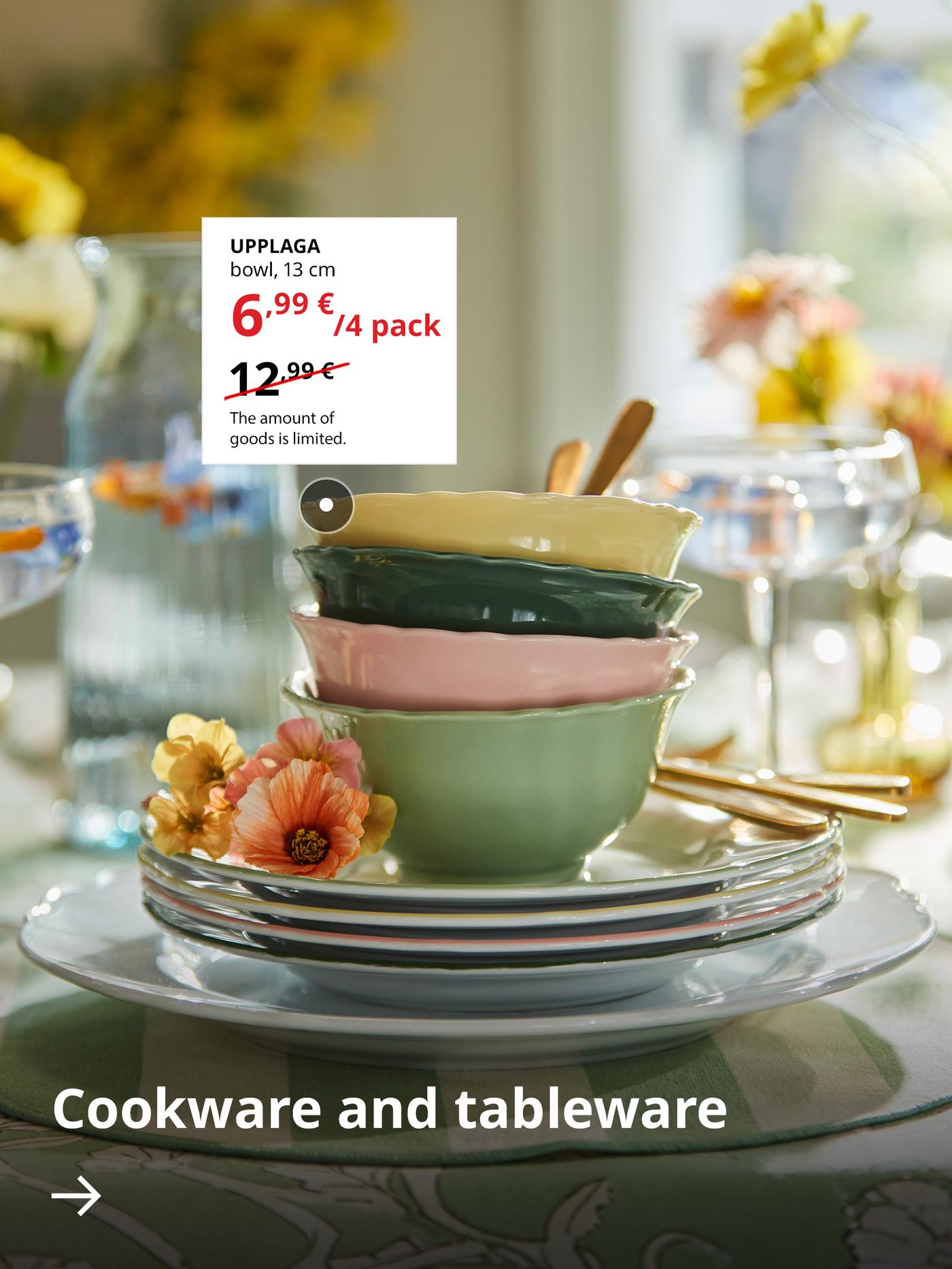 Stack of colorful ceramic bowls and plates on a beautifully set dining table with flowers and cookware, featuring an IKEA UPPLAGA bowl promotional offer.