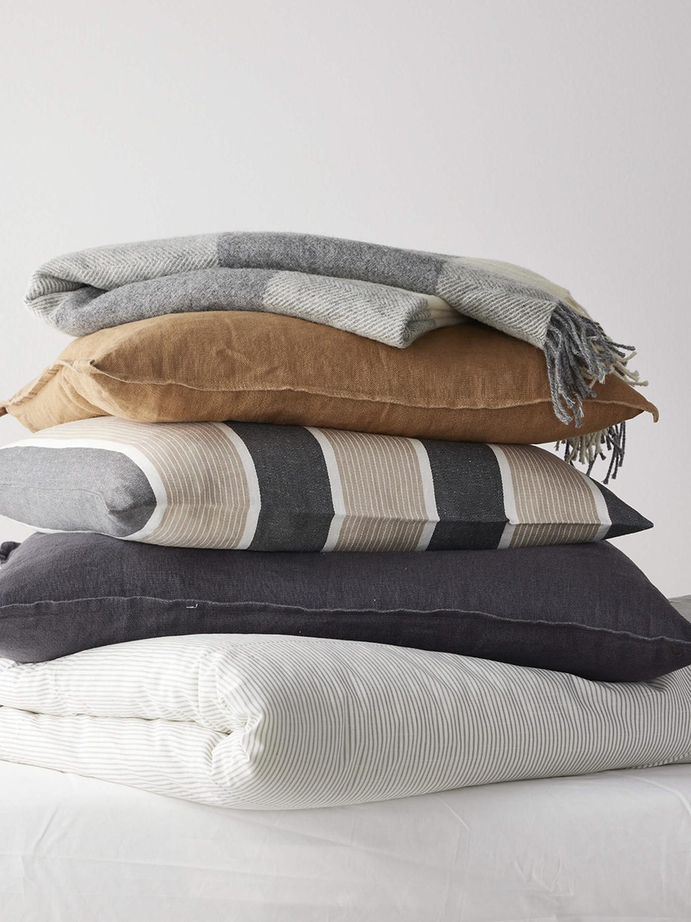 Stacked decorative pillows and a comforter with varying textures and colors.