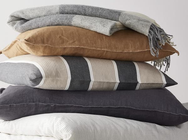 Stacked decorative pillows and a comforter with varying textures and colors.