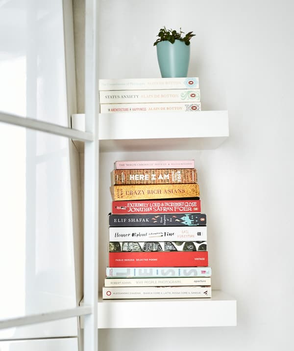 Stacks of books on miniature white shelves.