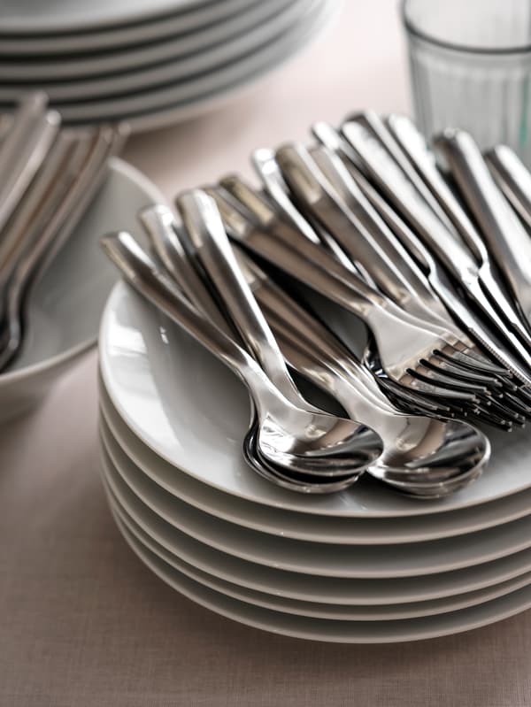 Stacks of plates, glasses, IKEA 365+ cutlery and other tableware on a tabletop with a beige tablecloth.
