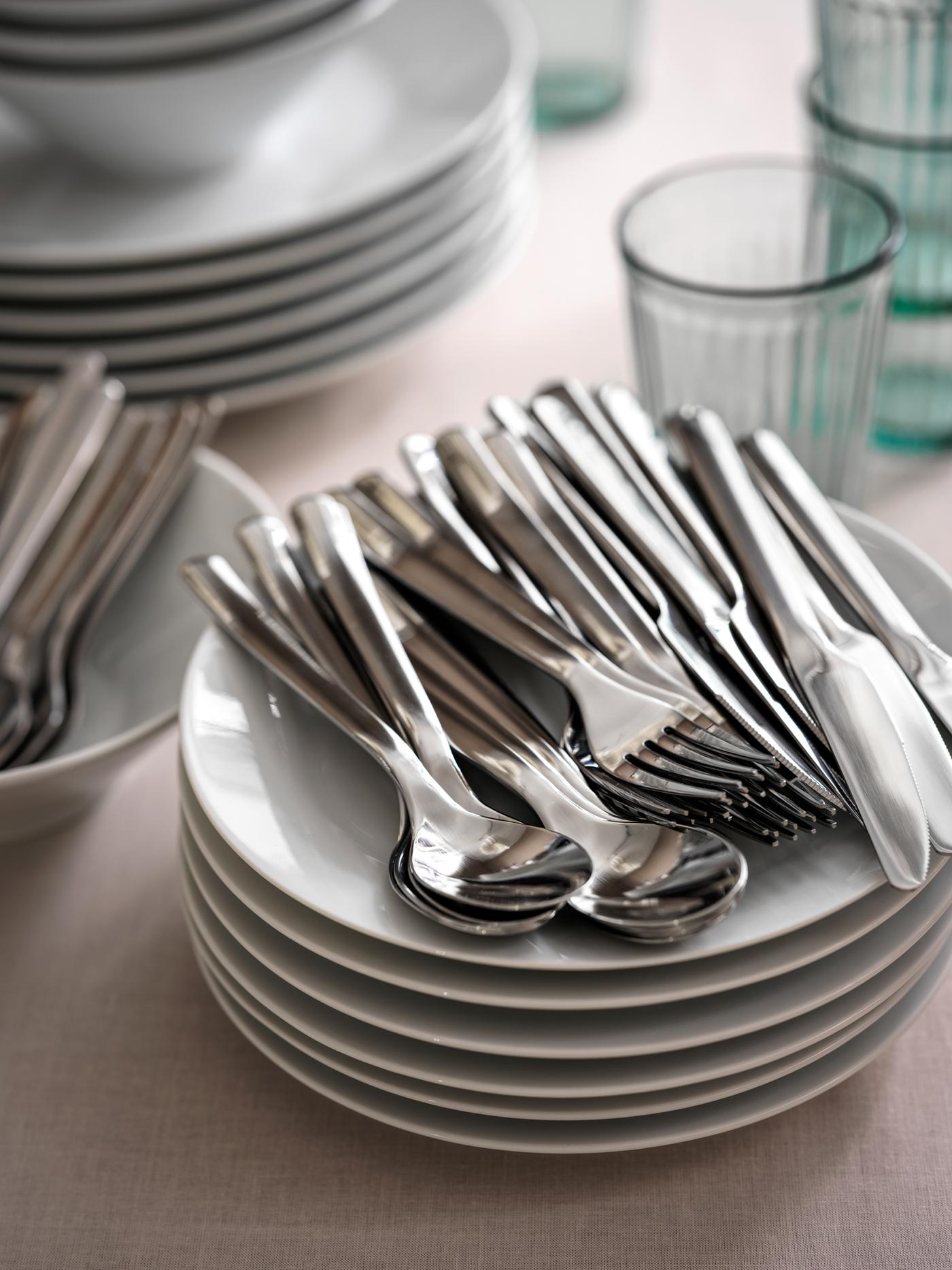 Stacks of plates, glasses, IKEA 365+ cutlery and other tableware on a tabletop with a beige tablecloth.