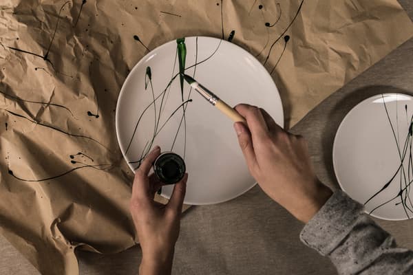 Stänkmålade vita tallrikar med grön färg och röd marmorerade vita muggar av nagellack. 
