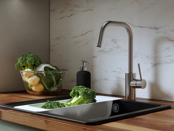 Stainless steel VIMMERN kitchen mixer tap with handspray on a round BOHOLMEN inset sink, green leaves on the edge.