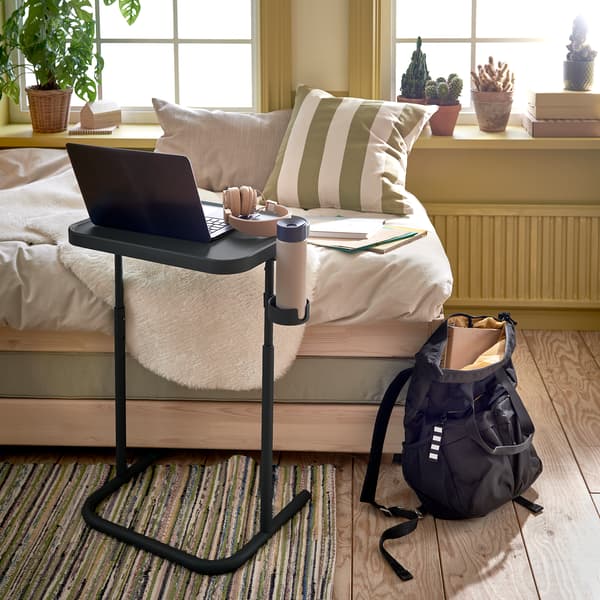 Standing between an armchair and window in a living room, a tray table is decked out for studying, including drink and fruit.