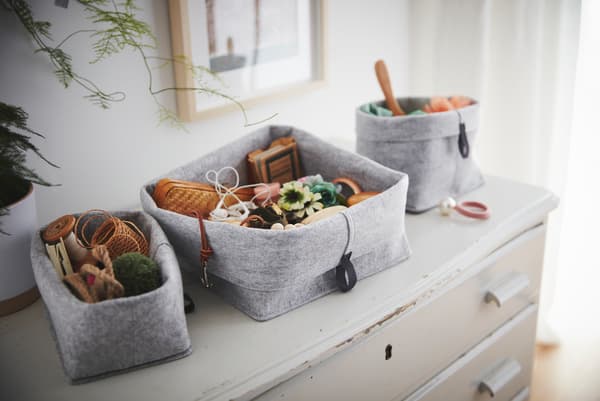 Standing on an old, worn chest of drawers is a set of RAGGISAR textile baskets, filled with trinkets and clutter.