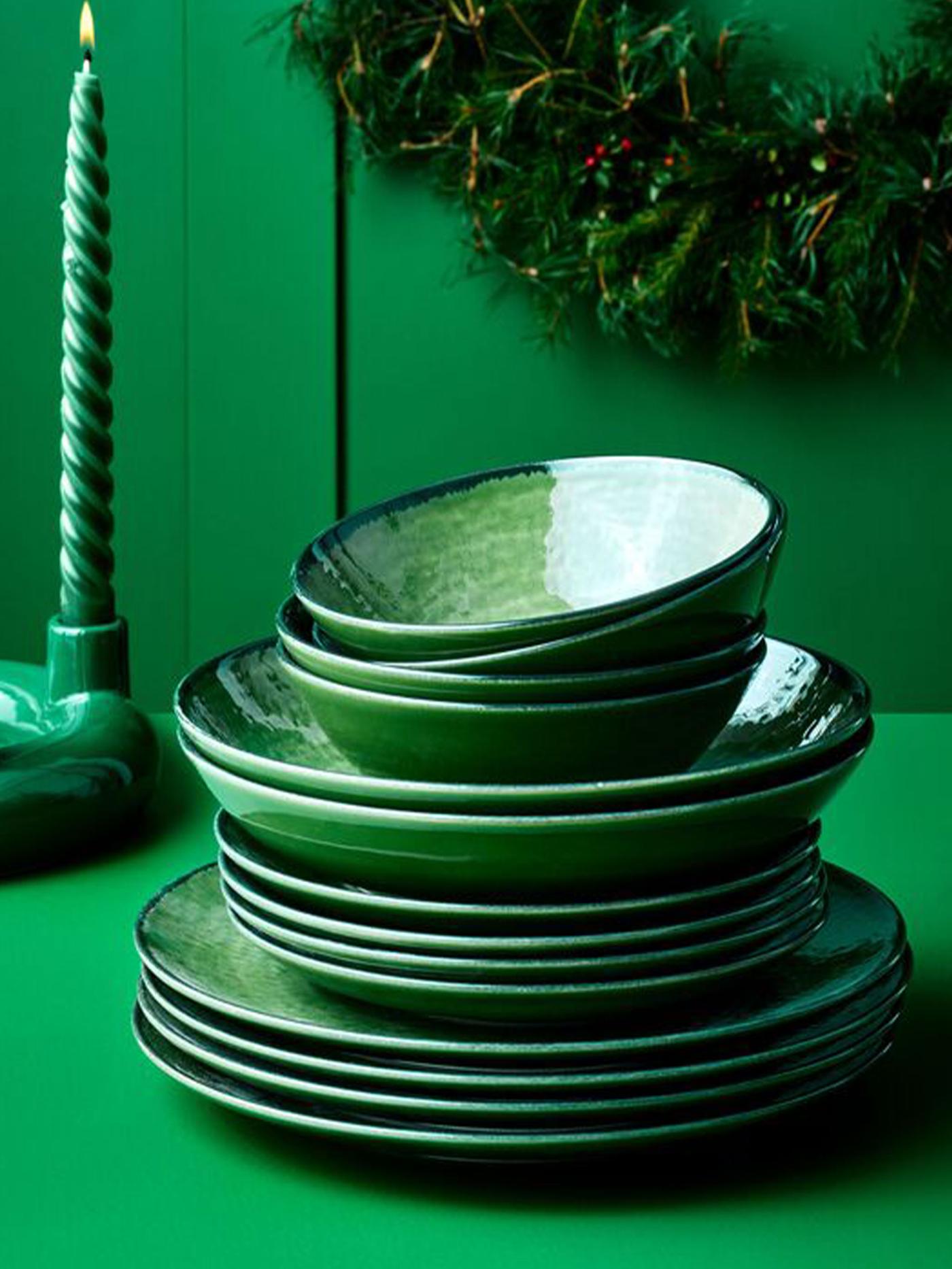 Staplade gröna tallrikar och skålar på ett grönt bord, med en grön ljusstake i bakgrunden.