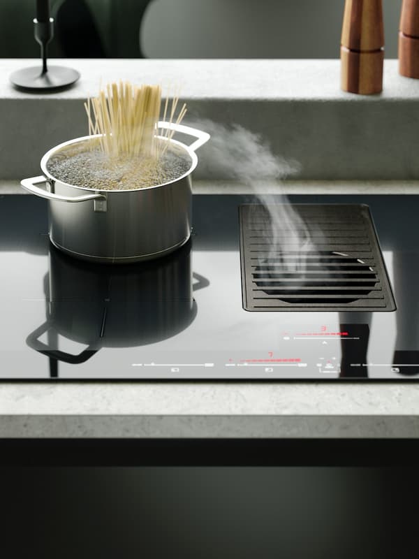 Steam rises from boiling pasta water in a pot and goes into integrated extractor on a black FORNEBO induction cooktop.