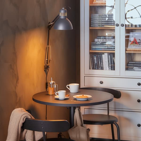 STENSELE café table with two chairs, two white coffee mugs on the table, and behind it a white bookcase with glass doors.