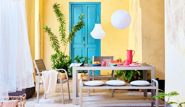 Stimmungsbild eines Balkontisches mit Sitzbank und 2 Stühlen vor einer Wand in Apricot und mit blauer Holztür