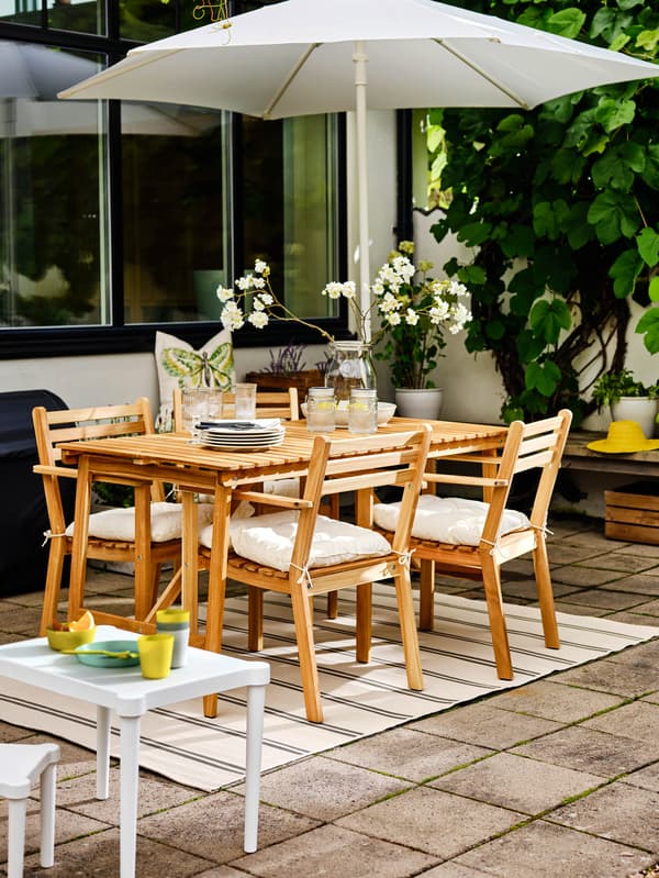Stôl a stoličky s opierkami ASKHOLMEN stoja v záhrade pod slnečníkom HÖGÖN.