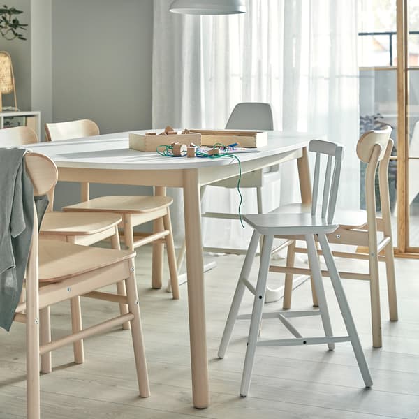 Stół do jadalni, krzesła z brzozowego drewna, krzesełko do karmienia i krzesło dla dziecka z oparciem na stopy. Na stole leżą dziecięce materiały do prac ręcznych.