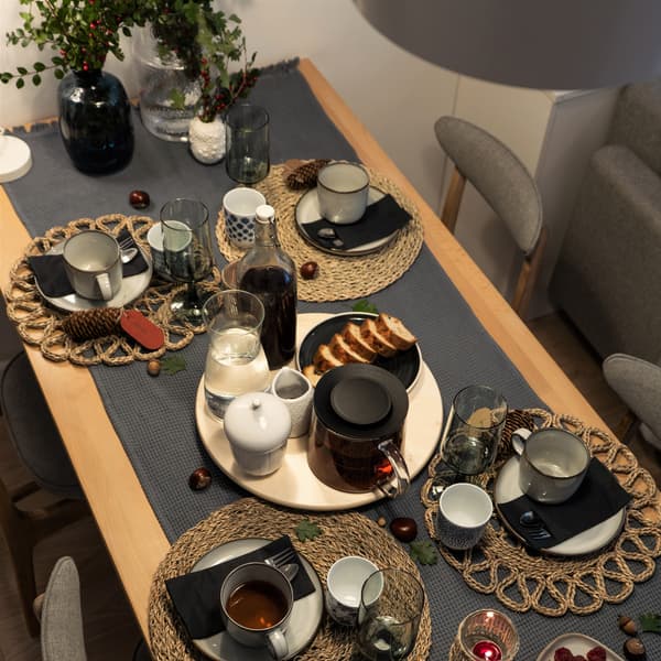 Stół jadalni zastawiony zastawą stołową i taca na środku z herbatą w dzbanku i karafką wody.