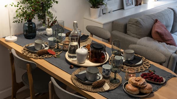 Stół jadalni zastawiony zastawą stołową i taca na środku z herbatą w dzbanku i karafką wody.