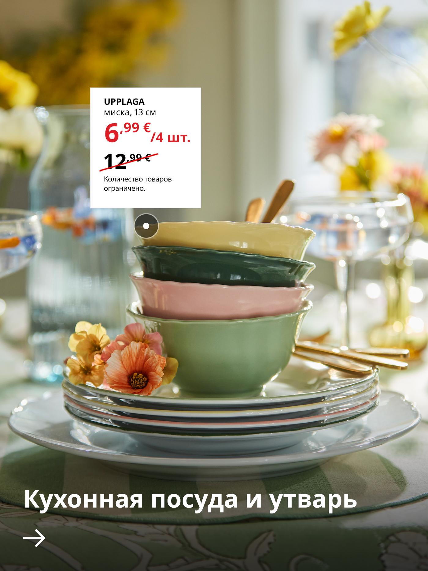 Стопка разноцветных керамических мисок и тарелок на красиво сервированном столе с цветами и кухонной посудой, демонстрирующая специальное предложение на миски IKEA UPPLAGA.
