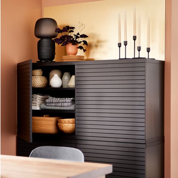 Storage behind anthracite doors, a brass-coloured wall panel, a black lamp, candles and a purple plant.