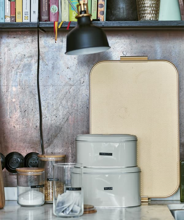Storage jars, tins and a tray against a copper wall.