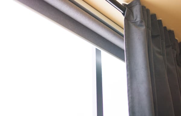 Store connecté FYRTUR gris enroulé, derrière un rideau gris.