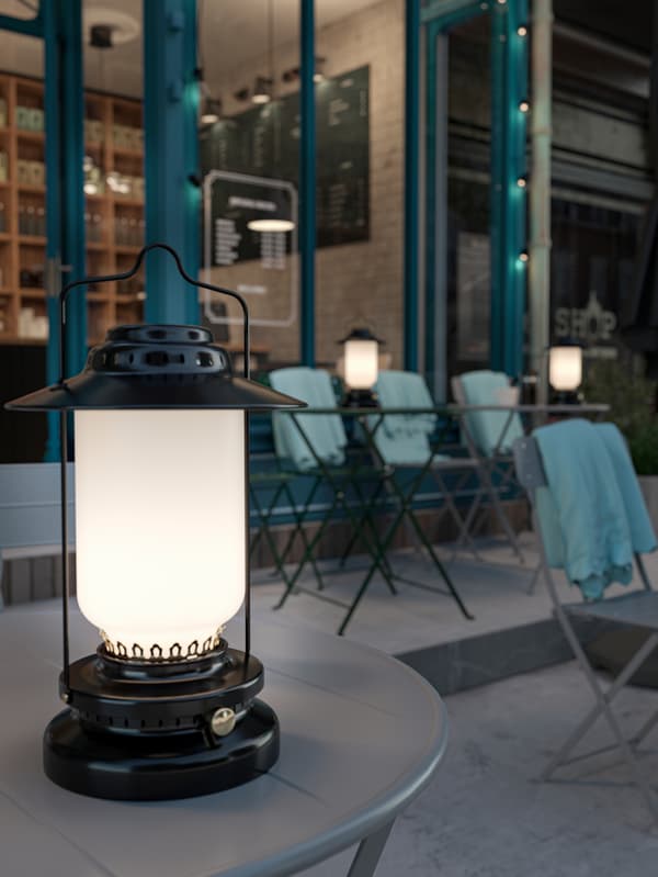 STORHAGA ledlampen op grijze SUNDSÖ tafels buiten bij een café, met lichtblauwe THORGUN plaids over de rugleuningen van de stoelen.